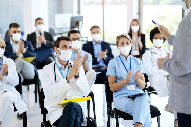Profissionais de saúde e empresários usando máscaras faciais e aplaudindo em um seminário