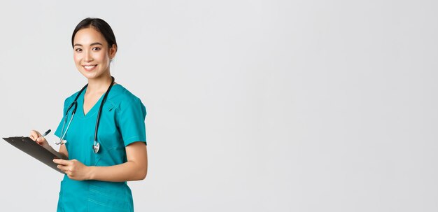 Profissionais de saúde, prevenindo vírus, conceito de campanha de quarentena. Sorrindo amigável médica, enfermeira em jaleco escrevendo análise de resultados na área de transferência, fundo branco de pé.