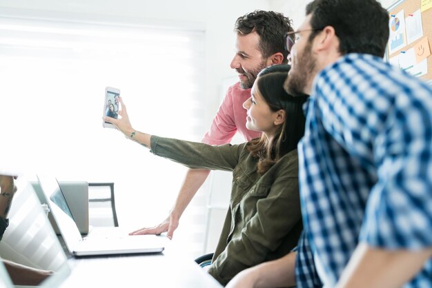 Profissionais masculinos e femininos tomando selfie no smartphone no local de trabalho