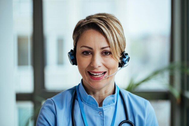 Profissional de saúde sorridente usando fone de ouvido enquanto conversa com um paciente e trabalha no call center do hospital