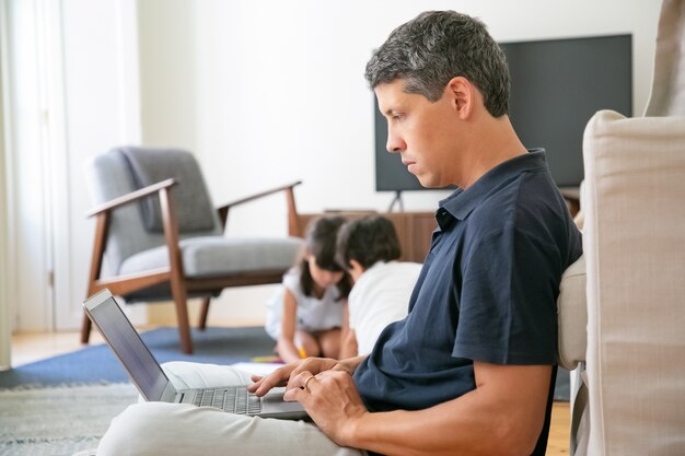 Profissional sério trabalhando em casa, sentado no chão e usando o laptop