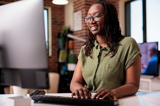 Programador afro-americano sorridente relaxando olhando para conteúdo engraçado na tela do computador enquanto digita no teclado. freelancer rindo com amigos enquanto conversa usando pc na sala de estar de casa.