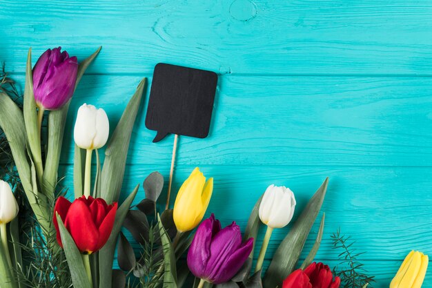 Prop preto em branco do discurso com tulipas coloridas no pano de fundo de madeira turquesa