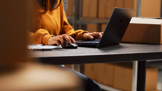 Foto grátis proprietário de inicialização trabalhando no inventário de estoque com laptop, planejando a distribuição de pedidos para gerenciamento de negócios na sala de armazenamento. trabalhador que faz o envio da cadeia de suprimentos na mesa, produtos de varejo. tiro portátil.