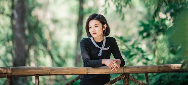 Protrait jovem de pé na ponte de bambu sorri e parece uma bela natureza enquanto acampa na floresta com espaço de cópia feliz