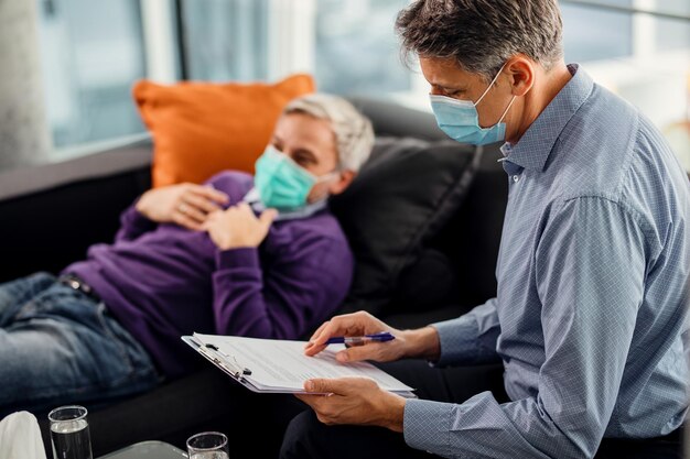 Psiquiatra masculino passando por dados de seu paciente enquanto tem consulta durante a pandemia de coronavírus