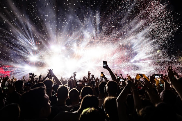 Público animado assistindo fogos de artifício de confete e se divertindo no festival de música à noite copiar espaço