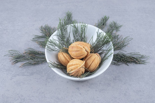 Punhado de biscoitos recheados de caramelo, adornados com folhas de pinheiro na mesa de mármore.