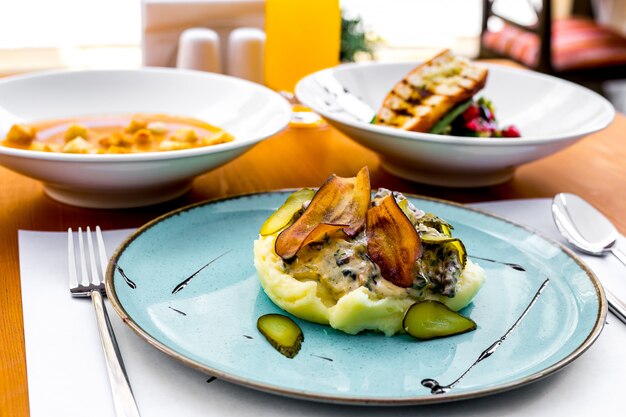 Purê de batatas com berinjela frita, picles e molho de natas em um prato