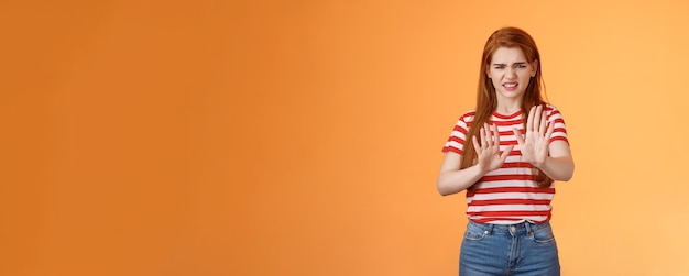 Foto grátis puxa, fede mulher ruiva exigente e enojada bloqueando o sinal levante as mãos na defensiva fazendo careta