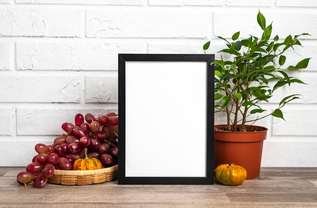 Quadro em branco ao lado do vaso de flores e uvas