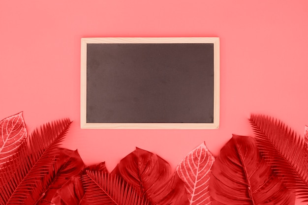 Foto grátis quadro-negro em branco com folhas de coral contra fundo rosa