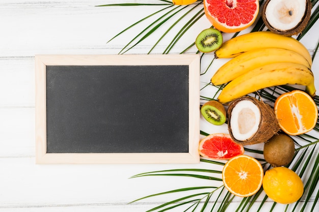 Foto grátis quadro-negro perto de folhas de plantas com frutas tropicais frescas