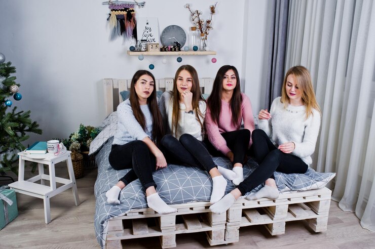 Foto grátis quatro amigas fofas usam suéteres quentes e calças pretas na cama no quarto decorado de ano novo no estúdio