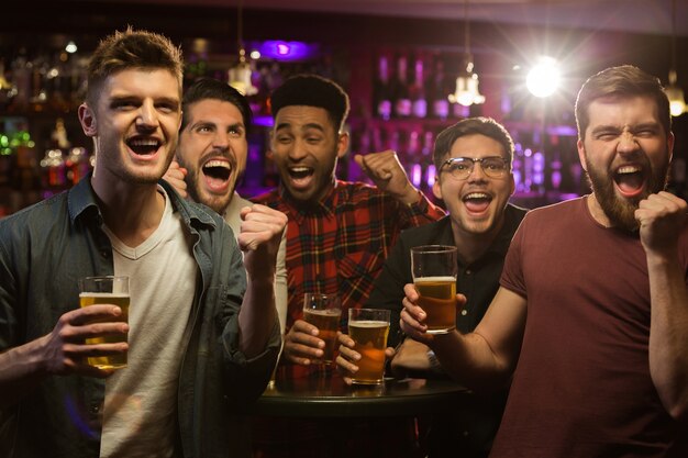 Quatro homens felizes segurando canecas de cerveja e gesticulando