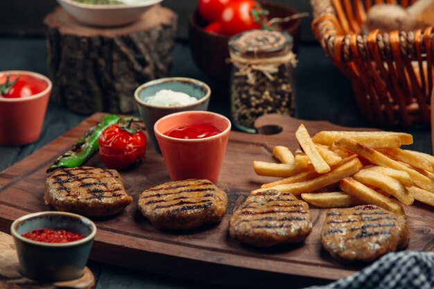 Quatro pedaços de rissóis de bife grelhado com batatas fritas, maionese, ketchup, legumes grelhados