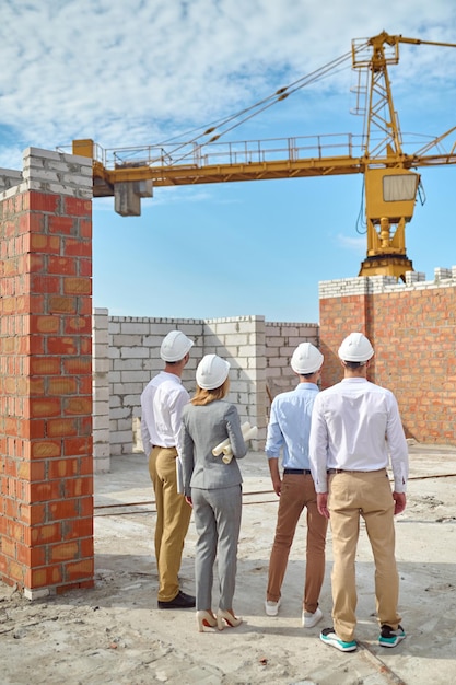 Quatro pessoas em capacetes de proteção inspecionando a área de construção