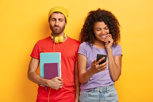 Que bom casal elegante posando contra a parede amarela com gadgets