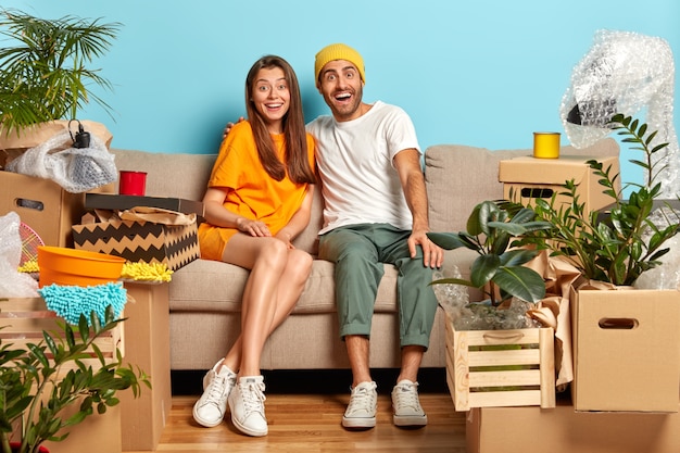 Que bom que marido e mulher olham com felicidade, se abraçam enquanto estão sentados no sofá da sala, mudam-se para a nova casa, caixas de papelão ao redor