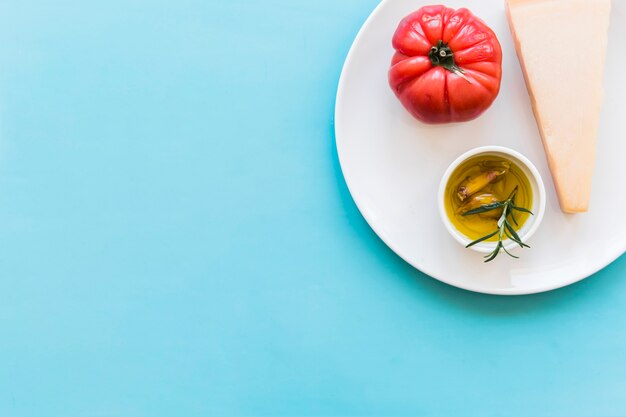 Foto grátis queijo cheddar triangular com tomate vermelho e alho óleo de erva luva e alecrim na placa