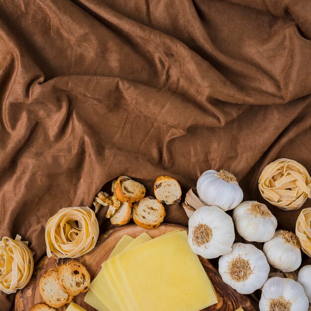 Queijo fatiado, macarrão cru, pão e alho em pano marrom