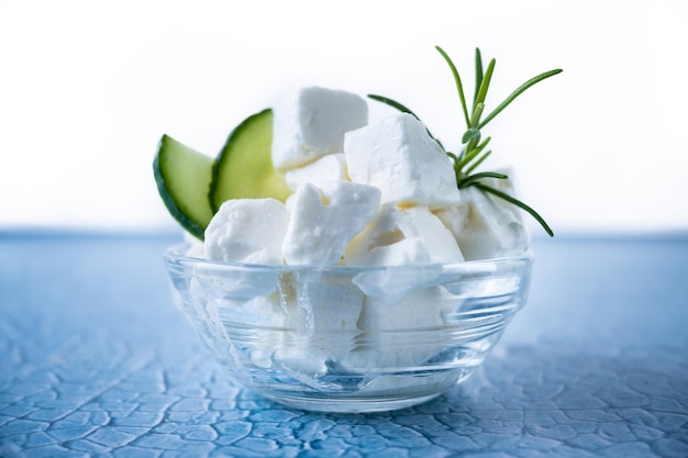 Queijo feta pepino e ervas em uma tigela sobre fundo azul