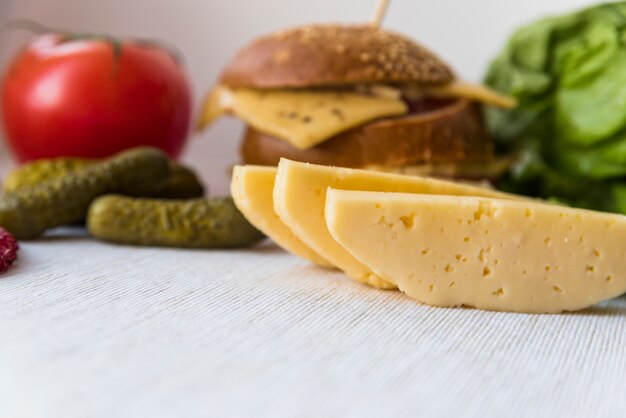 Queijo fresco perto de tomate, pepino e sanduíche na mesa