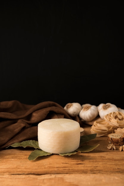 Queijo manchego espanhol, folhas de louro, macarrão cru e alho lâmpadas na mesa de madeira