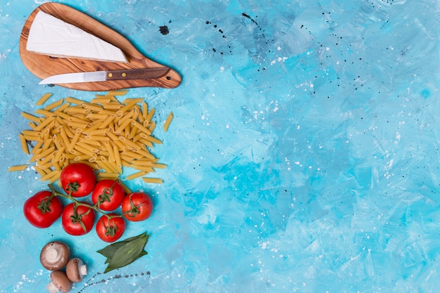 Foto grátis queijo; massa de penne; tomates vermelhos; cogumelo e folhas de louro na superfície azul