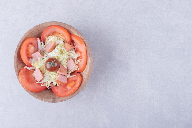 Queijo ralado com salsichas e tomates em uma tigela de madeira.