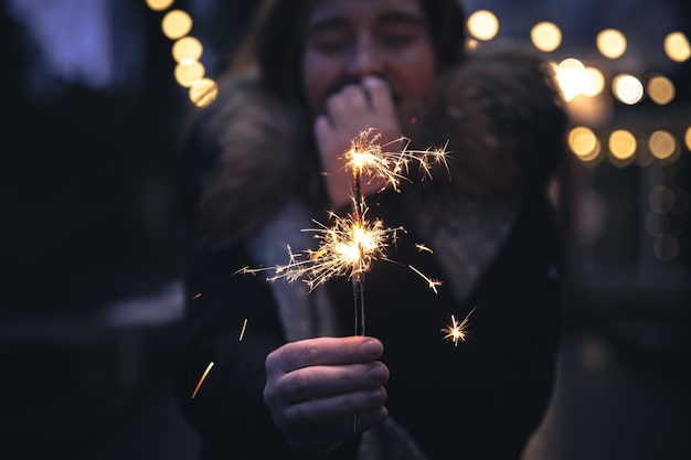 Queimando fogos de artifício nas mãos de uma jovem no escuro