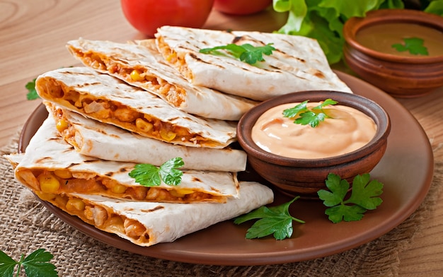 Quesadilla mexicano fatiado com legumes e molhos em cima da mesa