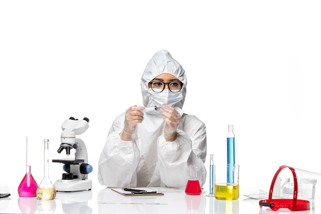 Química feminina com um traje de proteção especial segurando uma injeção na mesa branca e branca. Química do vírus covid pandemia