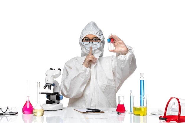 Química feminina de frente para o químico em traje de proteção especial segurando frascos vazios na mesa branca.