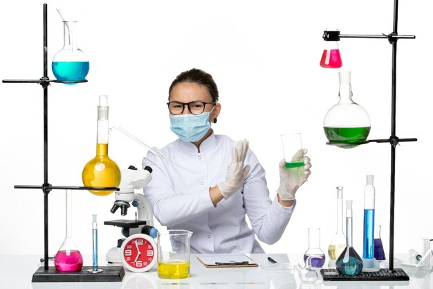 Foto grátis química feminina de frente para o terno médico com máscara segurando a solução no fundo branco respingo laboratório vírus química covid