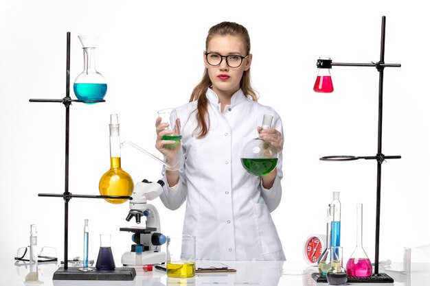 Química feminina de frente para o terno médico segurando o frasco com solução verde sobre fundo branco claro.