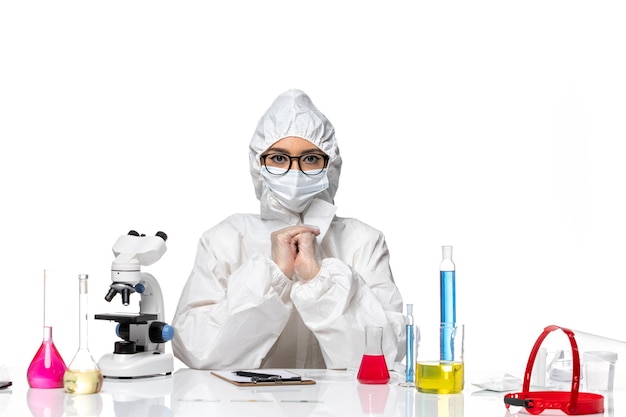 Química feminina em traje de proteção especial sentada de frente com soluções no fundo branco. Química, vírus covid, pandemia