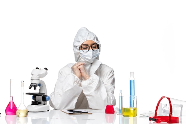 Química feminina em traje de proteção especial sentada de frente com soluções sobre fundo branco claro. Química, vírus covid, pandemia