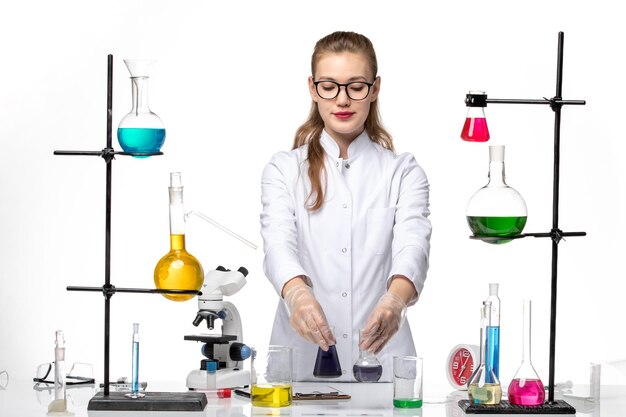 Química feminina em traje médico de frente, trabalhando com diferentes soluções no vírus covidêmico da química da mesa branca