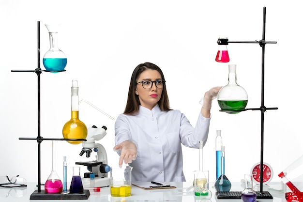 Química feminina em um terno médico branco sentada de frente no fundo branco.
