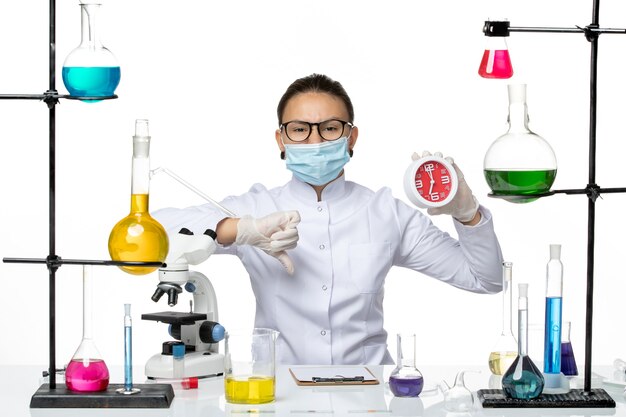 Química feminina vista frontal em traje médico com máscara segurando relógios vermelhos em fundo branco vírus laboratório química covid- splash