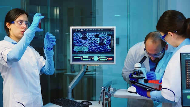 Químico sênior analisando amostra de sangue enquanto colegas de trabalho discutem