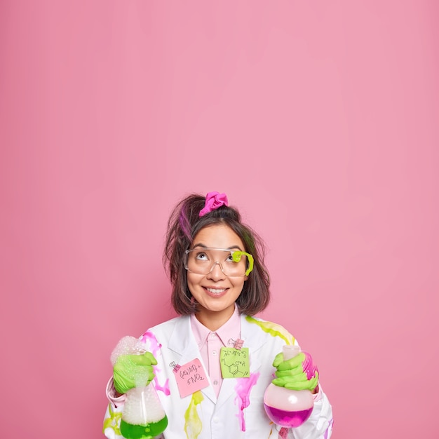 Foto grátis químico trabalha em laboratório de ciências conduz experimento químico segura frascos de vidro concentrados com expressão feliz acima isolados em rosa