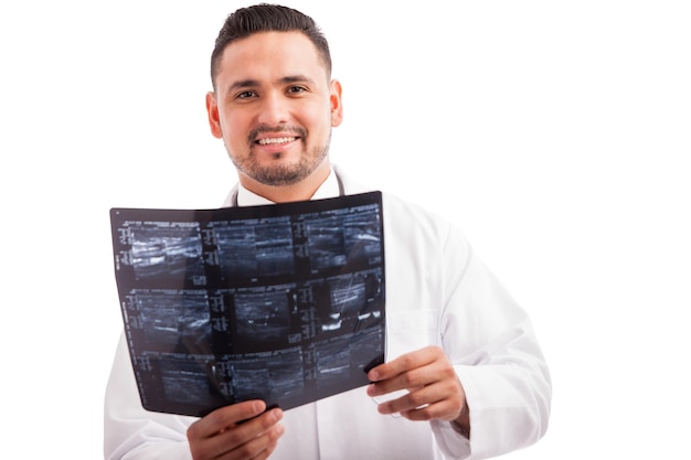 Radiologista hispânico jovem examinando alguns raios-x e sorrindo contra um fundo branco