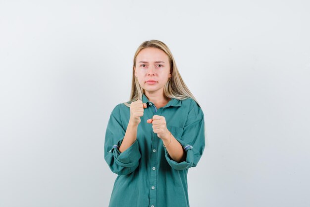 Rapariga loira com blusa verde em pose de boxeador e parecendo séria