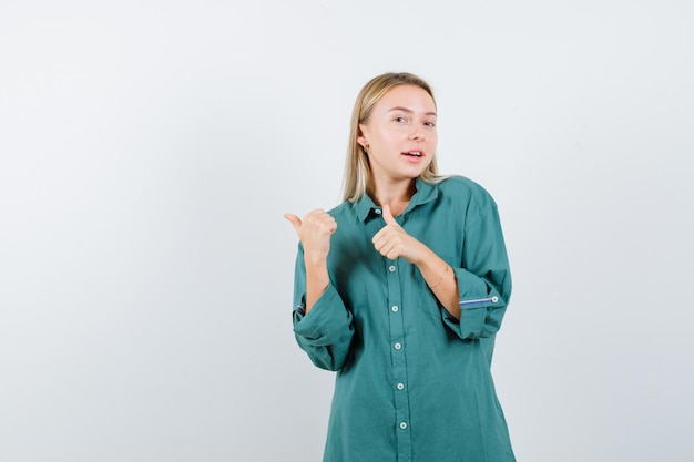 Rapariga loira com blusa verde mostrando os polegares para cima com as duas mãos e está bonita