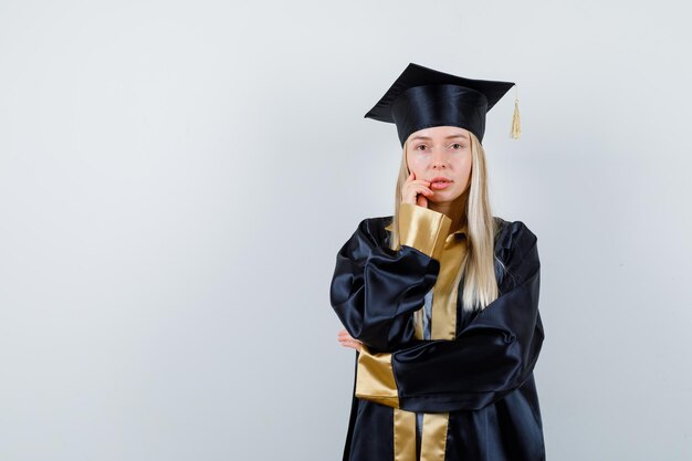 Rapariga loira com uniforme de pós-graduação em pose pensativa e parecendo sensata