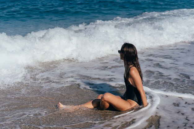 Rapariga loira em traje de banho sentado no bronzeamento de praia do mar