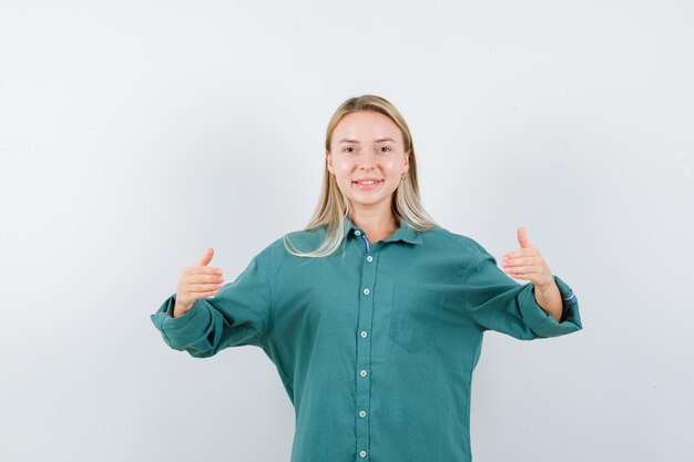 Rapariga loira esticando as mãos e segurando algo em uma blusa verde e parecendo feliz