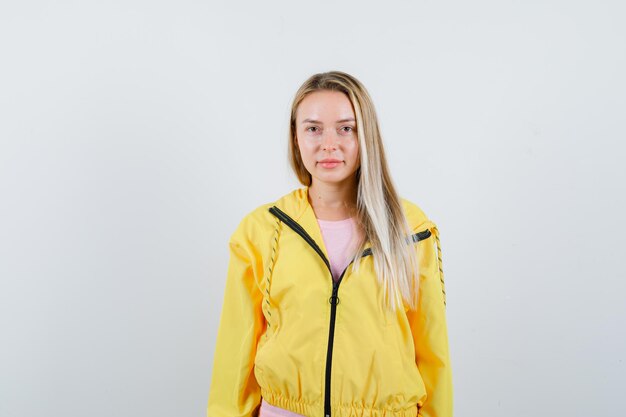 Rapariga loira olhando para a câmera com uma jaqueta amarela e linda